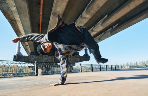 Young man break dancer dancing on urban background performing acrobatic stunts. Street artist