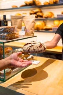 Hands of customer in the bakery shop buying an artisan bread from the baker in the workshop,