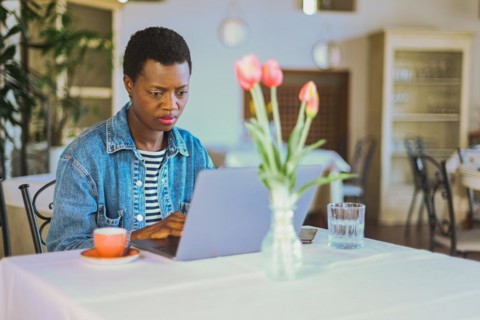 Woman using laptop with coffee cup and tulips on a table in sunlit restaurant