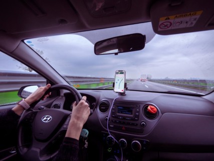 Driver's view from inside a car with a phone showing navigation on a cloudy day, A1 A8 highway near