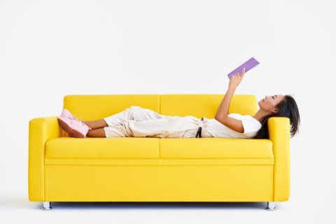 Pretty asian woman reading book lying at cozy yellow couch, concepts of home and comfort, hobby,
