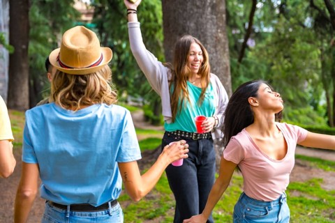 Multiethnic group of birthday party in the city park having fun and dancing with colored cups