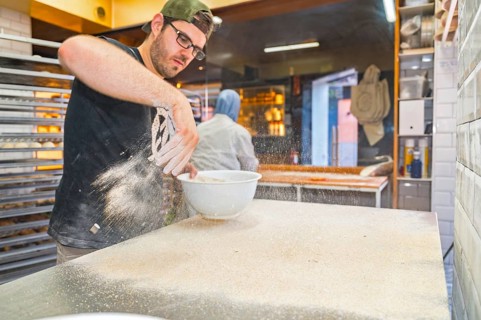 The employee placing flour in the dough of loaves before the oven in an artisan bakery workshop