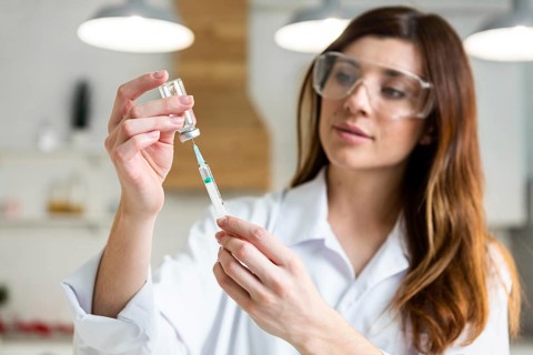 Female scientist with safety glasses holding syringe with vaccine lab