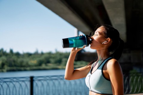 Young fitness woman drinking water from bottle. Sporty female resting after work out exercising in