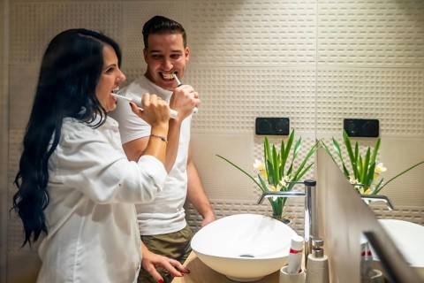 Side view of a happy couple brushing teeth together at home