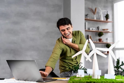 Smiley man working eco friendly wind power project while talking phone using laptop