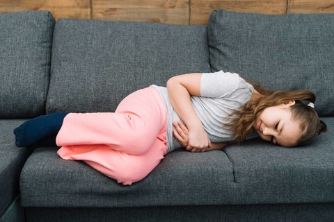 Little girl suffering from stomach ache lying gray sofa