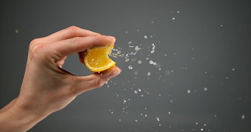 Hand of Woman Squeezing Orange against Black Background