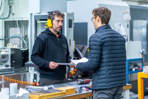 Two engineers talking while examining pieces in a cnc factory