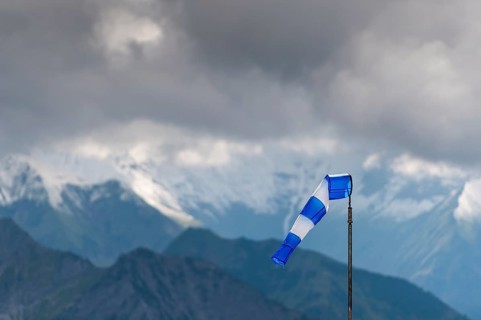 Blue and white windsock on the summit of the Nebelhorn in front of the mountain range with dark