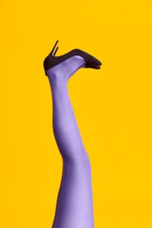 Raised females legs in bright tights and stylish high heels shoes on yellow background. Relax,