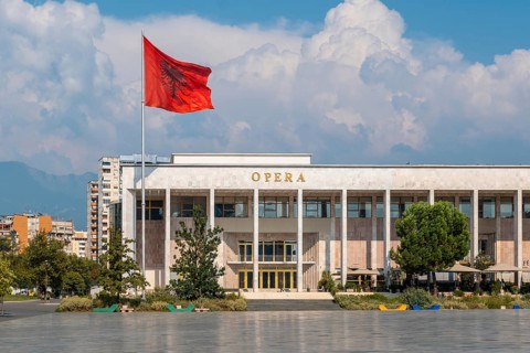 Palace of Culture or Opera on Skanderbeg Square in Tirana and the flag of Albania moving in the