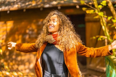 Woman with curly hair inhaling and closing eyes outdoors in a park in autumn