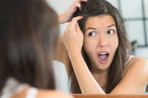 Horrified young woman looking in the bathroom mirror staring open mouthed at the first grey hair on