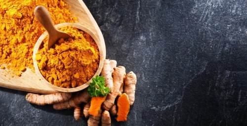 Composition with a bowl of ground turmeric and its fresh rhizome