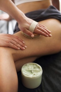 Unrecognizable female receiving anti cellulite massage with brush from professional masseuse in spa