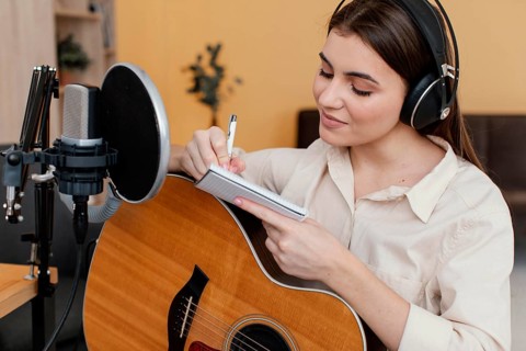 Female musician home writing song while playing acoustic guitar