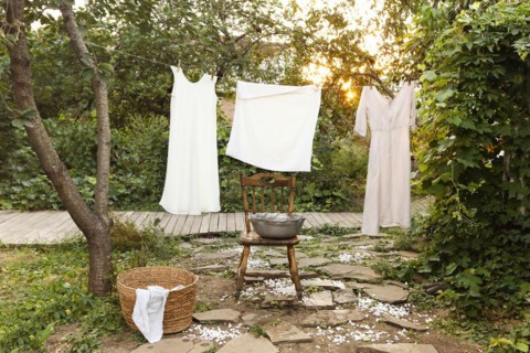 Clean wet garments hanging on rope and drying near retro chair and bowl on laundry day in garden