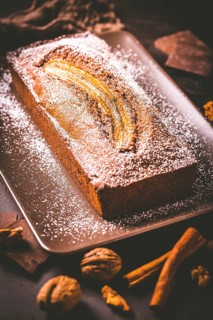 Homemade vegan banana bread or cake with nuts, chocolate and cinnamon on brown background