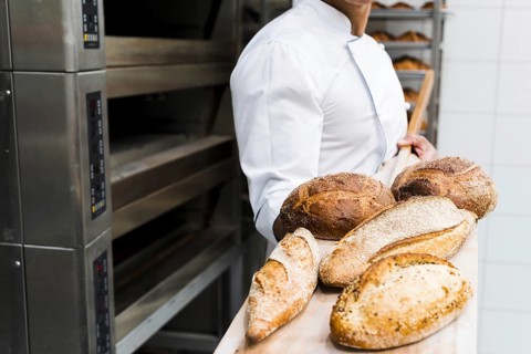 Close up male baker holding fresh baked bread wooden shovel from oven. High resolution photo