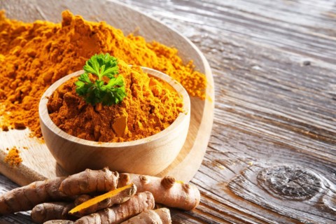 Composition with a bowl of ground turmeric and its fresh rhizome