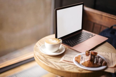 Freelance workplace in cafe. Table on coffeeshop with open laptop, newspaper and morning breakfast,