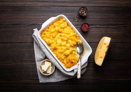 Close-up of baked mac and cheese in white casserole on rustic wooden background, with seasonings,