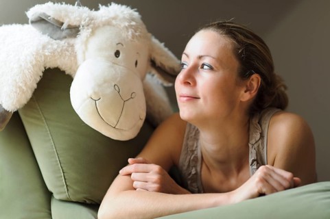 Young woman lying on the couch with a soft toy