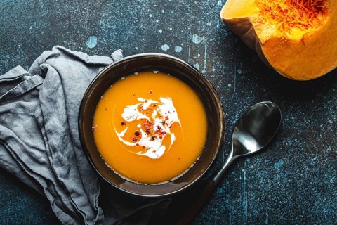 Homemade pumpkin cream soup served in brown ceramic bowl on dark stone background with spoon