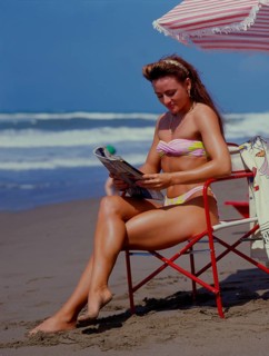 Young woman reading newspaper on beach, journal