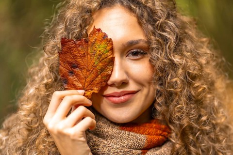 Close-up portrait of a beauty woman hiding one eye with a fallen leaf