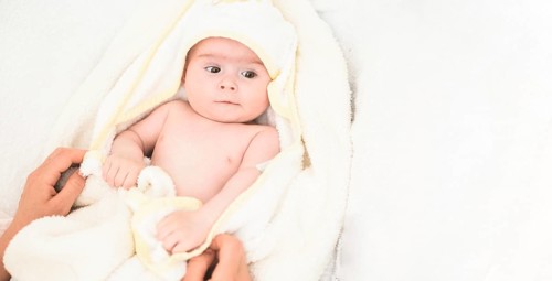Adorable 6 months old Baby girl infant on a bed on her belly with head up looking into camera with