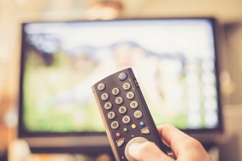 TV remote control in the foreground, tv in the blurry background. Film night with vod streaming