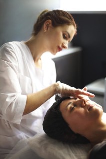 Vertical shot of professional beautician in medical gloves doing face massage for young woman in
