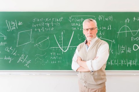 Elder professor standing near chalkboard classroom