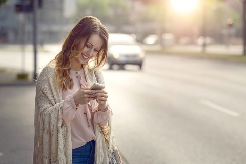 Attractive young woman checking a message on her mobile phone with a happy smile as she stands at