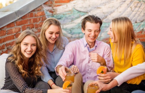 Group of young happy people friends drinking fruit cocktails together on house terrace, smiling and