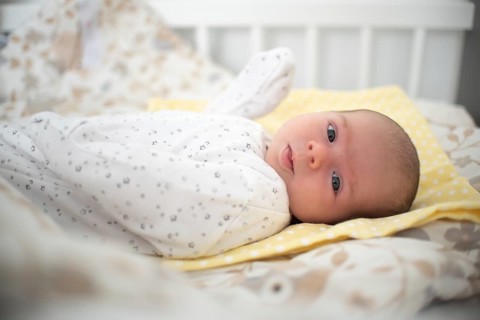 Newborn baby is lying on its side in baby crib in bright room