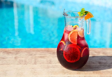 Glass jug of iced sangria with strawberry, orange, apple and lemon by the pool