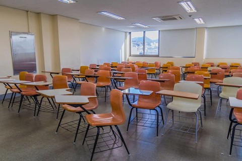 Classroom with empty desks arranged haphazardly with lights turned on and sunshine coming through