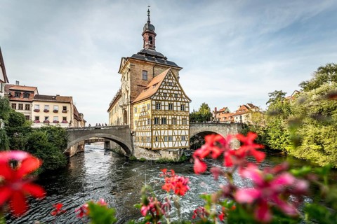 Colourful half-timbered house on a bridge with foreground of bright flowers over a river, old town