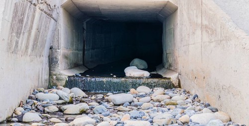 Concrete tunnel at Pebble Beach in South Korea with water running onto large rocks and stones,