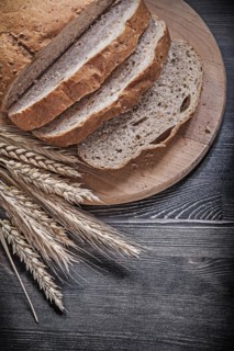Slices of baked bread on wooden carving board golden wheat rye ears food and drink concept