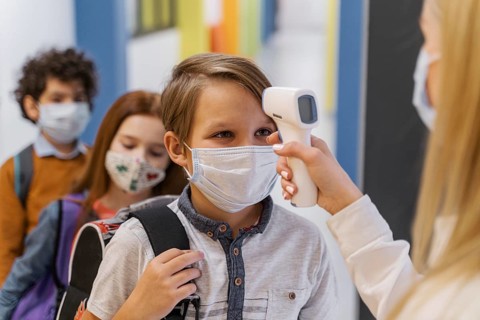 Female teacher with medical mask checking student s temperature school