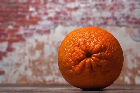 Close-up of a whole tangerine (oranges) (mandarins) (clementines) (citrus fruits) with a brick wall
