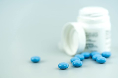 horizontal selective focus close up of white prescription pill bottle and blue pills