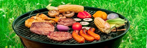Barbecue panorama. Grilled meat, sausages, chicken, vegetables, with green grass in the background