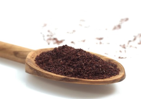 Sumac powder, spice in a spoon against white background