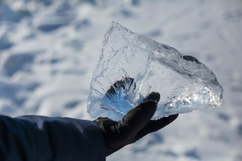 Happy smiling man wearing winter blue jacket and holding piece of transparent crushed ice cubes in